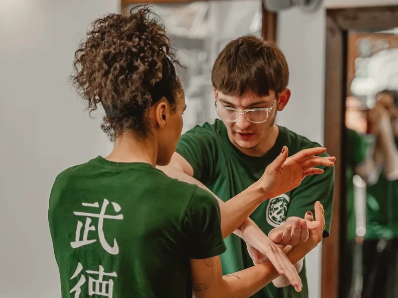Twee leden in groene WuDae-shirts oefenen samen een Wing Chun-handtechniek