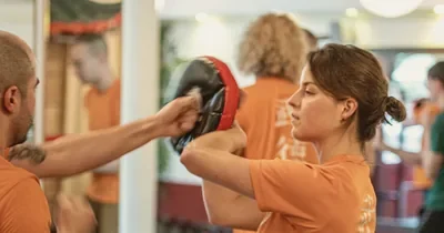 Lid in oranje WuDae-shirt stoot op een stootkussen tijdens de les